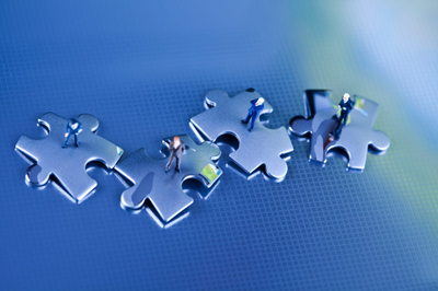 linkedin group Four puzzle pieces are arranged in a line with miniature figurines of people standing on top of each piece against a blue background.
