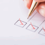 A hand holding a pen checks boxes on a checklist, with several boxes already marked with red check marks.