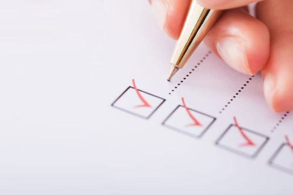 A hand holding a pen checks boxes on a checklist, with several boxes already marked with red check marks.